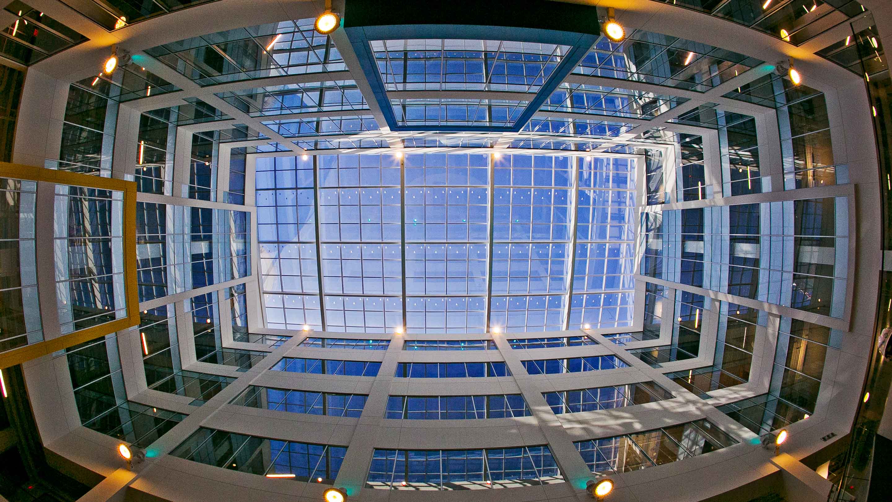 Looking up towards a glass ceiling of a multi-floor building atrium. 